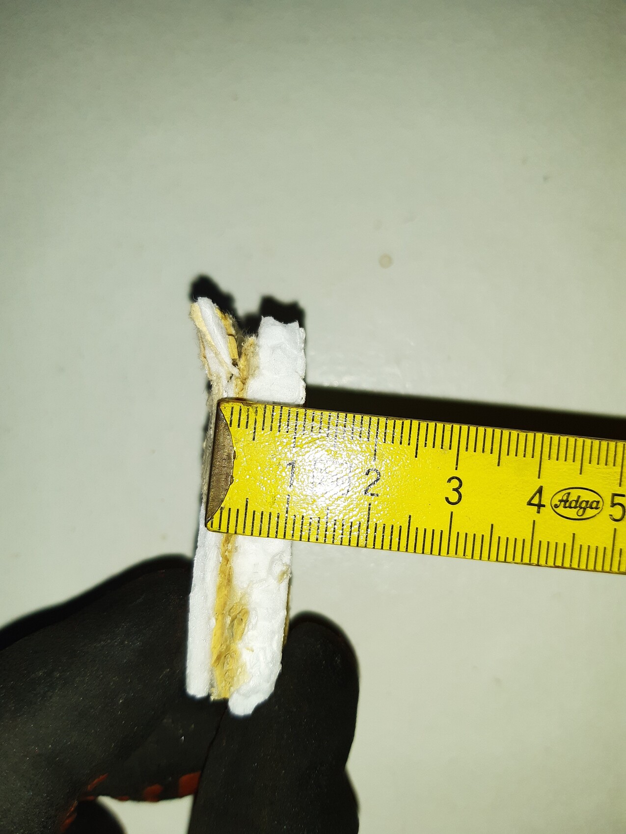 Nahaufnahme eines weißen Putzstücks neben einem gelben Maßband, ca. 3 cm lang.