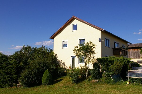 Zweistöckiges gelbes Einfamilienhaus mit Garten, Bäumen, Sträuchern und Satellitenschüssel.