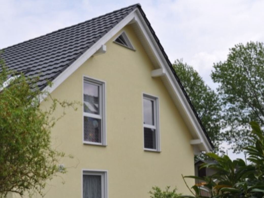 Gelbes Einfamilienhaus mit Satteldach, zwei oberen Fenstern, von Bäumen umgeben.