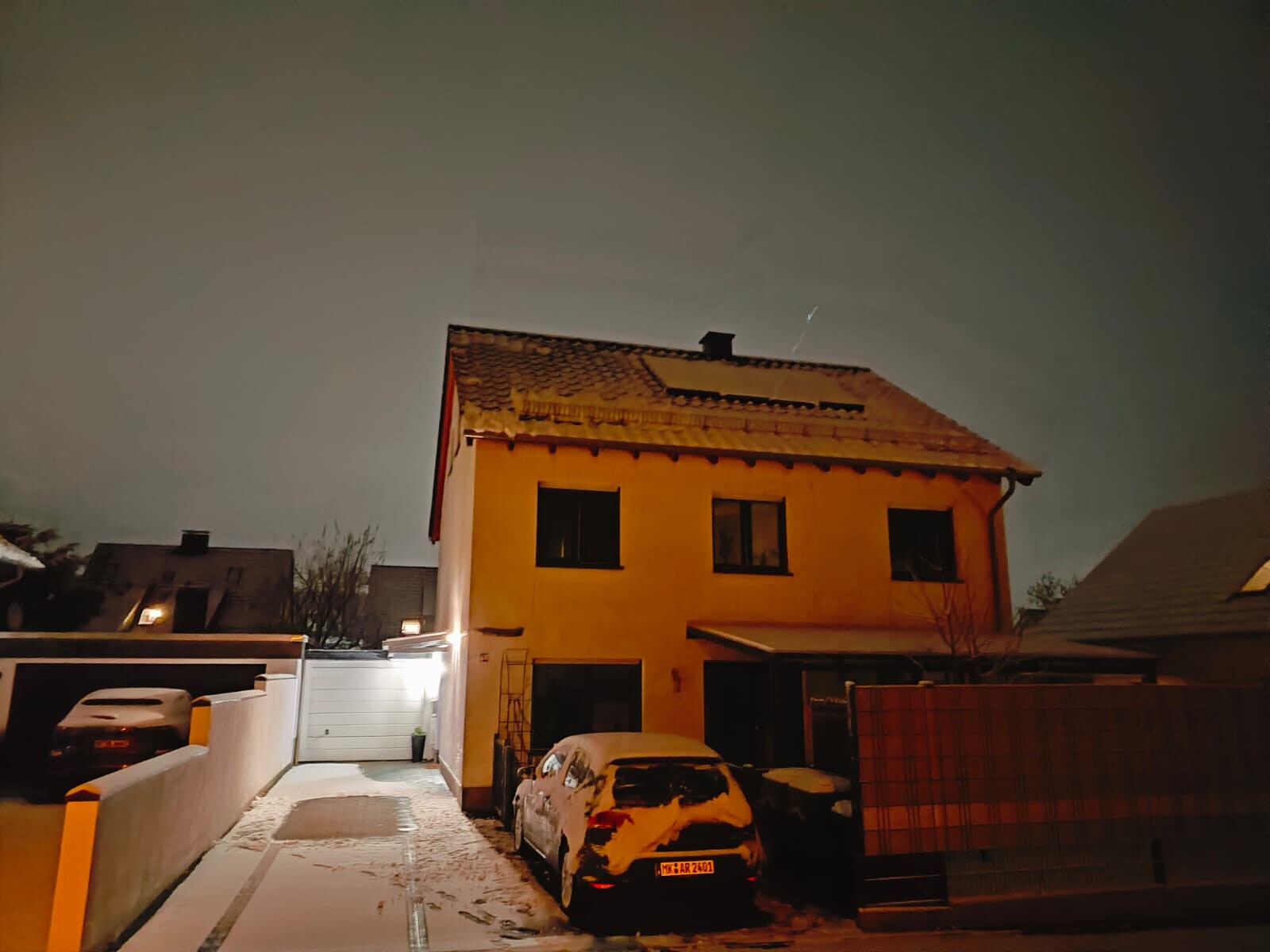 Gelbes zweistöckiges Haus mit Ziegel-Dach, Schnee vor Einfahrt, geparkte Autos