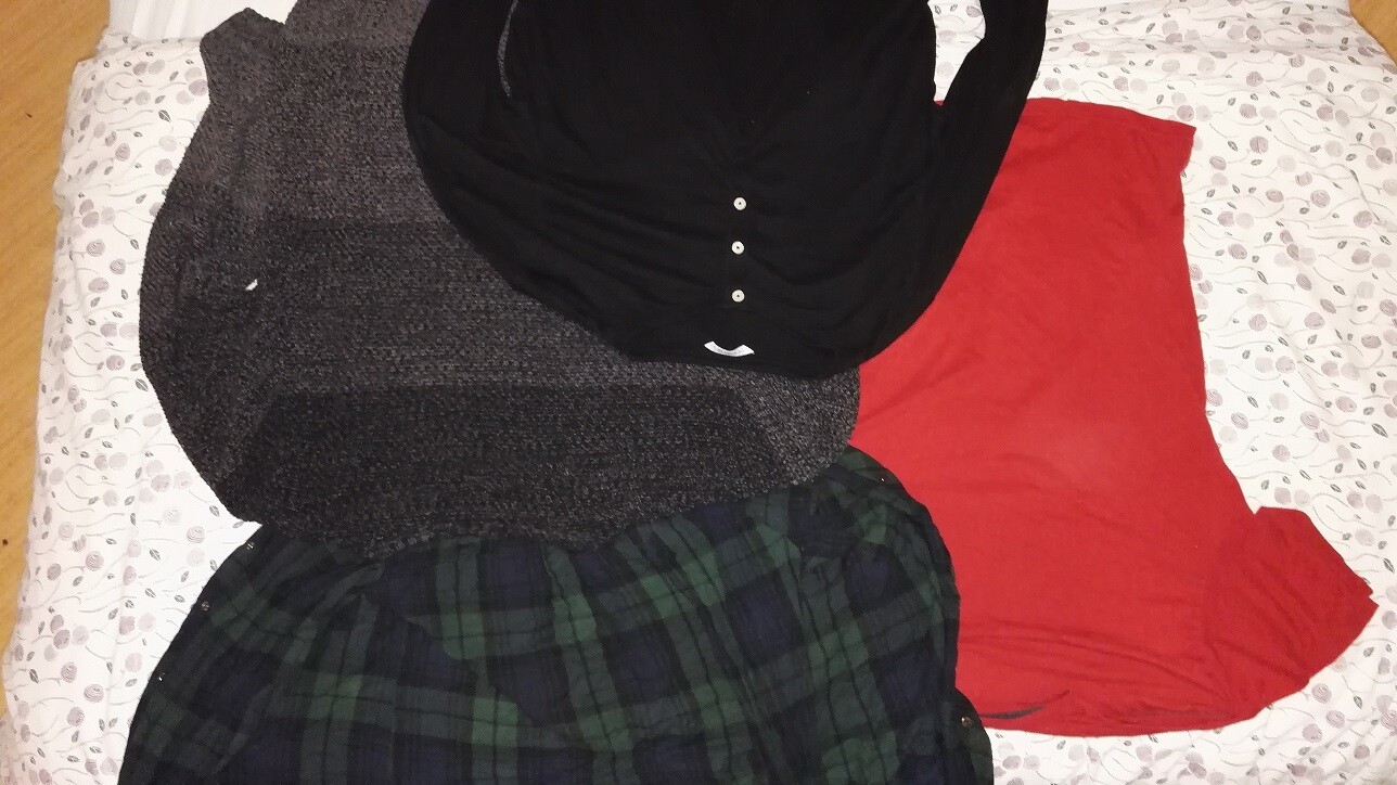 Kleidungsstücke liegen auf dem Bett: schwarzes Oberteil, graue Jacke, roter Stoffrock