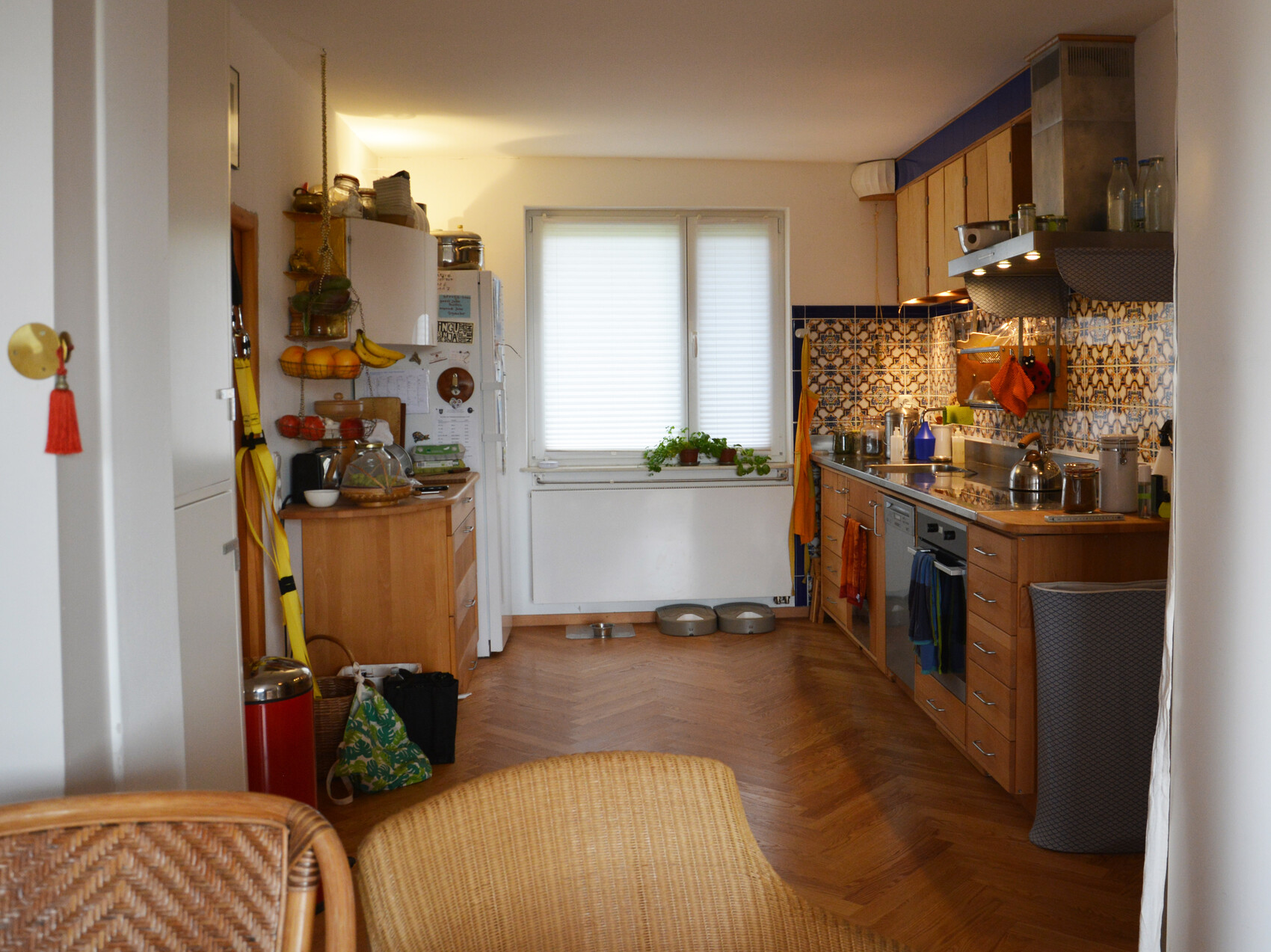 Küche mit Holzboden, rechte Küchenzeile, bunte Fliesen hinter dem Herd, Fenster in der Mitte