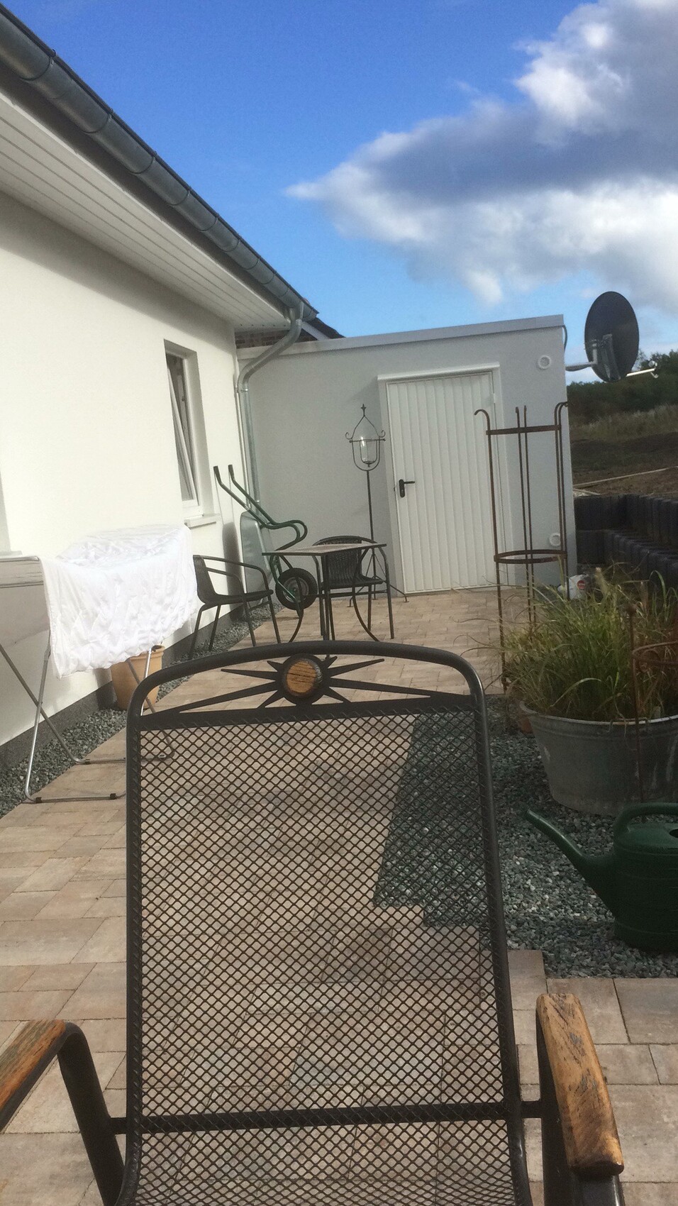 Terrasse vor weißem Haus mit Metallstühlen, Wäscheleine und Pflanzkübel.