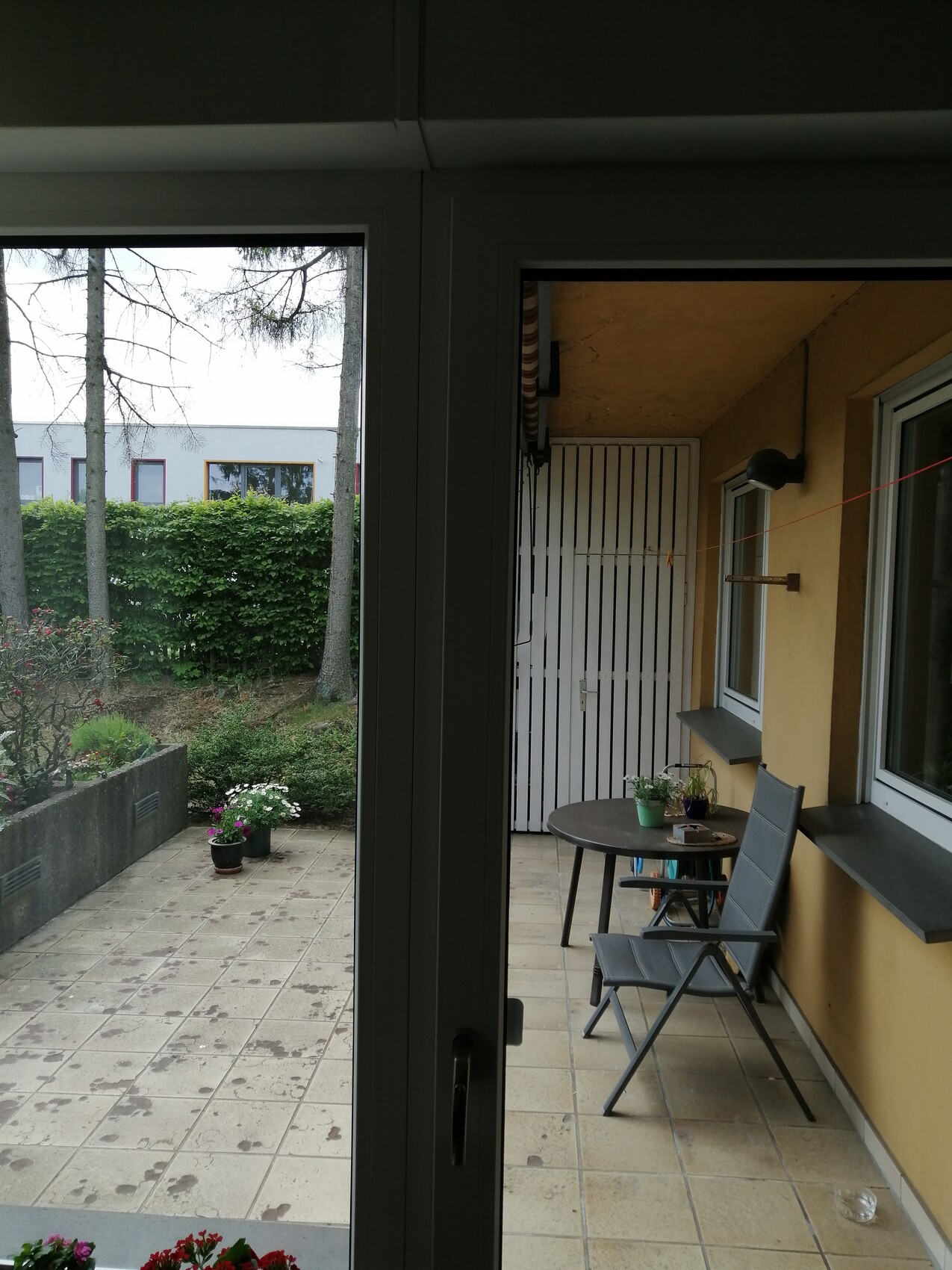 Balkon/Veranda mit rundem Tisch, zwei Klappstühlen, Topfpflanzen; Blick auf Garten.