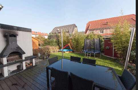 Gemuetliche Terrasse mit Esstisch, Stuehlen, Grill und Garten im Hinterhof.