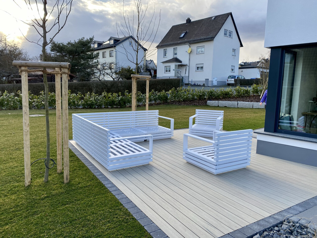 Weiße Holz-Gartenmöbel auf hellen Terrassendielen vor modernem Haus; Sitzgruppe im Garten.