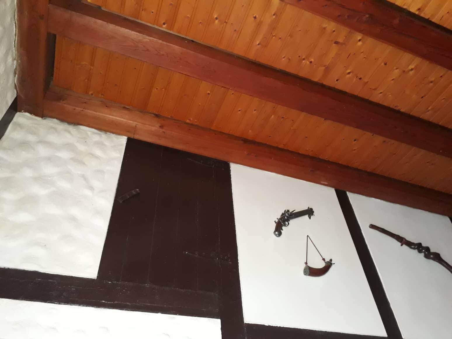 Dachboden mit Holzbalkendecke; weiße Wandpaneele, darauf antike Waffen wie Pistolen ausgestellt.