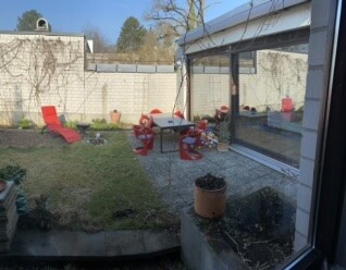 Gartenbereich mit roten Stuehlen, Tisch, Glastuer und gruenem Rasen