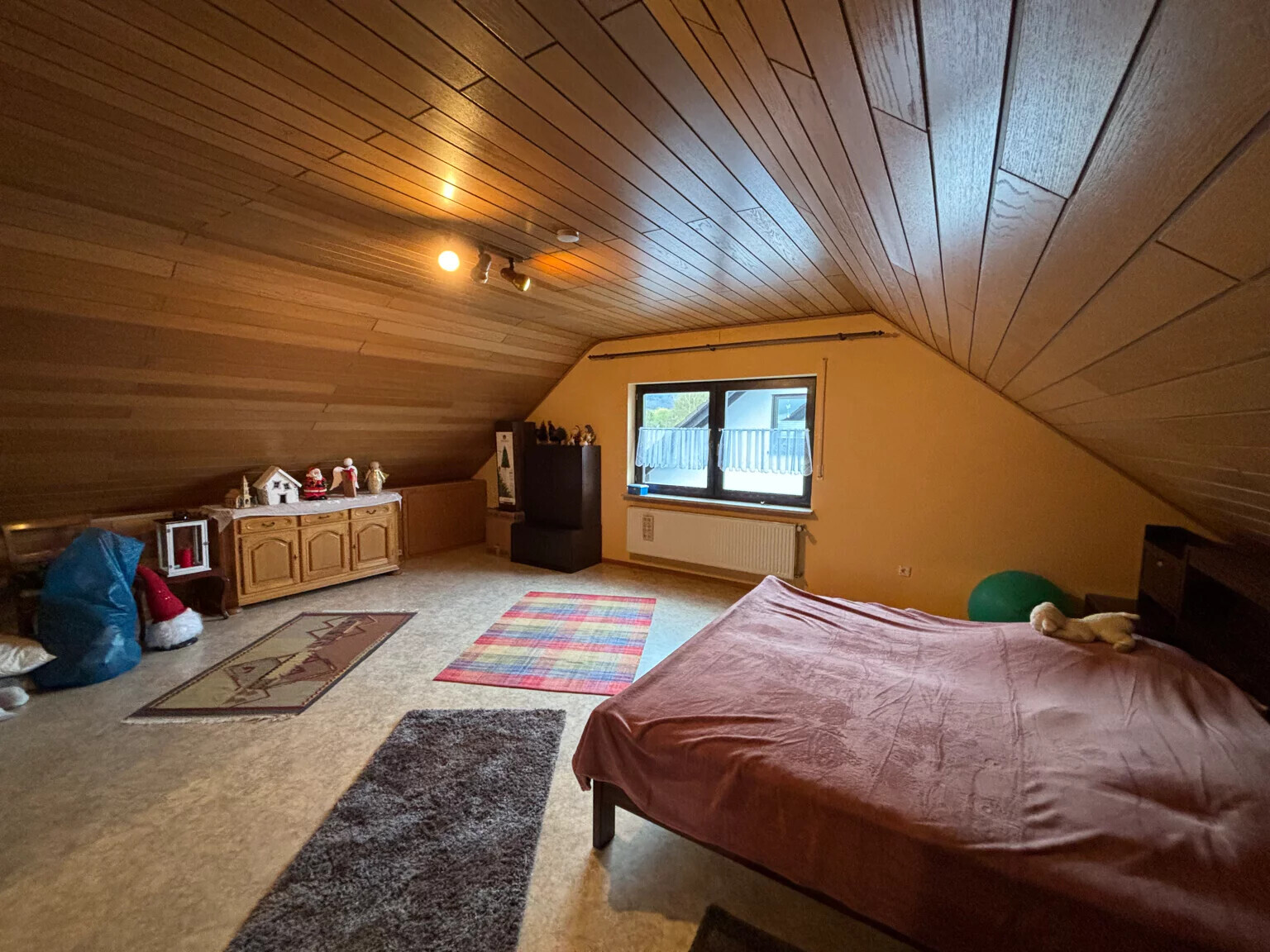 Dachgeschoss-Schlafzimmer: Bett mit rosa Decke, Fenster, Heizkörper und Spielzeug.