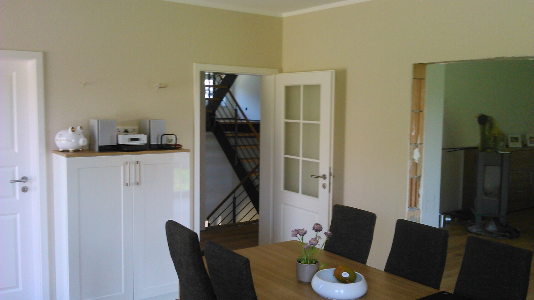 Esszimmer mit Esstisch, grauen Stühlen, weisser Schrank, Treppe hinter offener Tür.