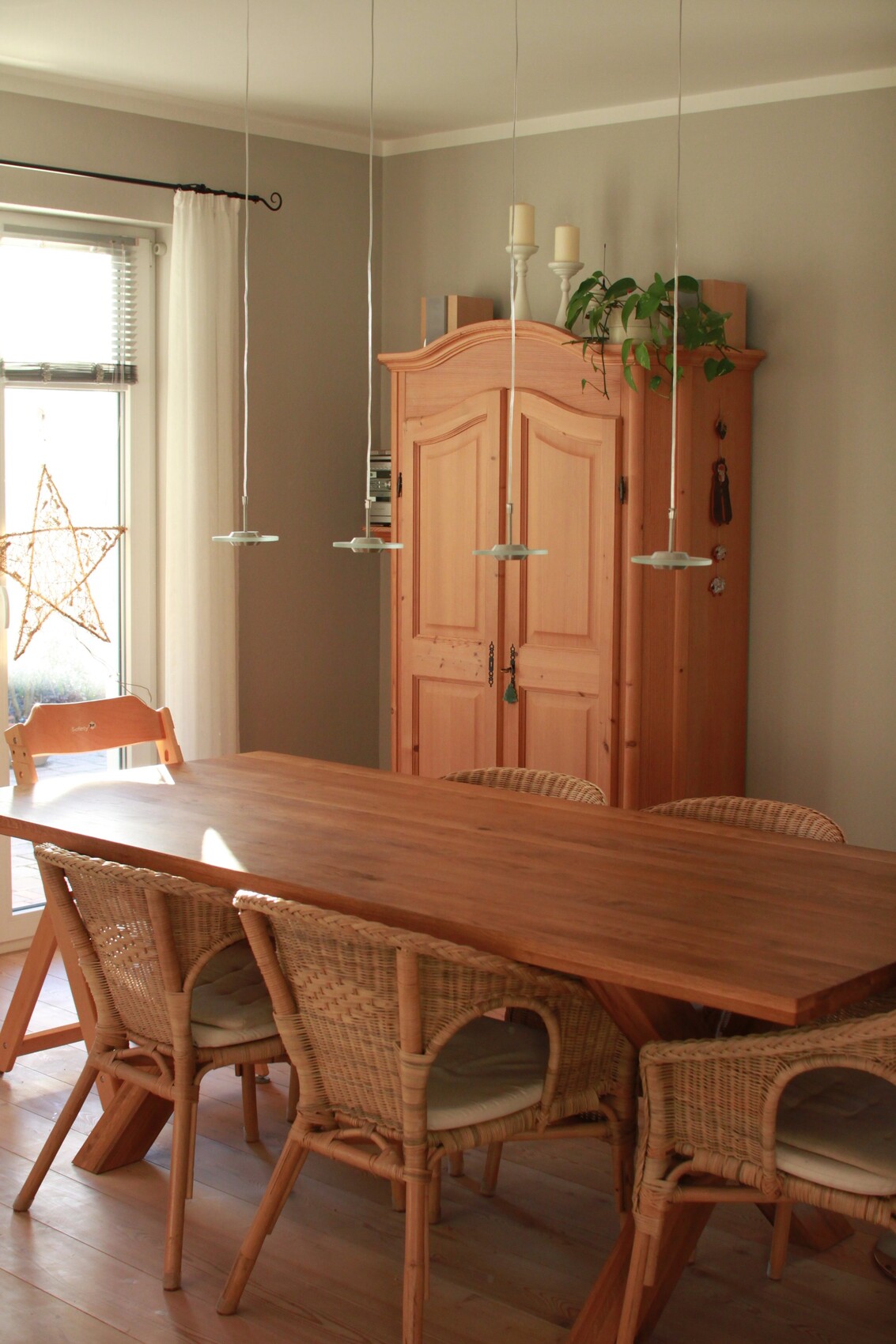 Helles Esszimmer: Holztisch mit Korbstühlen, großer Holzschrank, Pflanze und Fensterdeko.