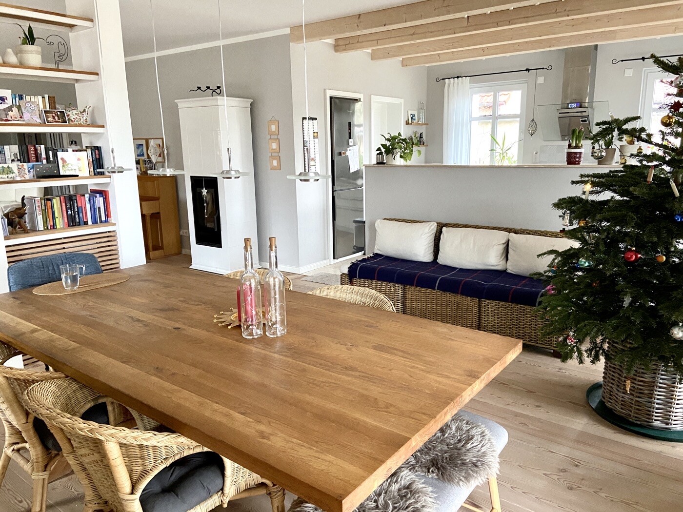 Heller offener Wohn- und Essbereich: Holztisch, Korbstühle, Sofa, Kamin, Weihnachtsbaum.
