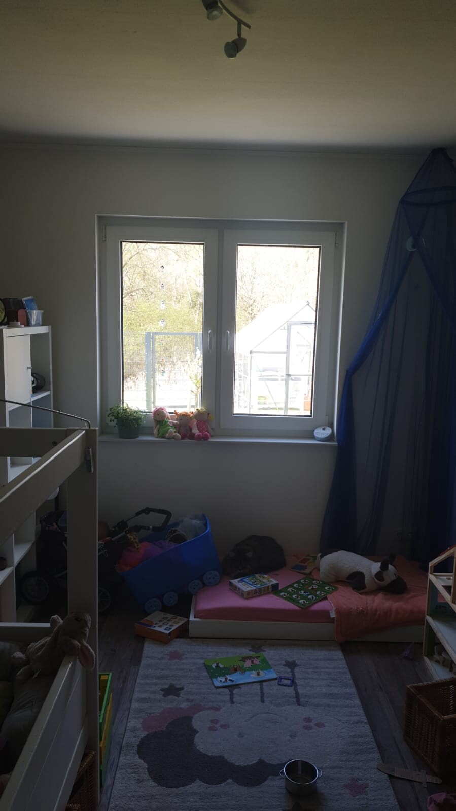 Kleines Kinderzimmer: Fensterfront mit Kuscheltieren auf der Fensterbank, Spielmatte und blaues Zelt.