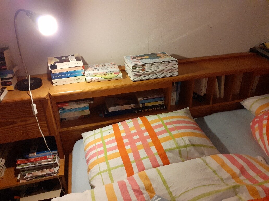 Holzregal mit Büchern, Leseleuchte links, Bett mit bunten Kissen