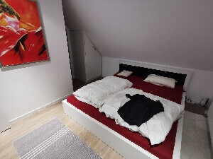 Schlafzimmer mit weißem Bett, rotem Bezug, Kleiderschrank und Wandbild.