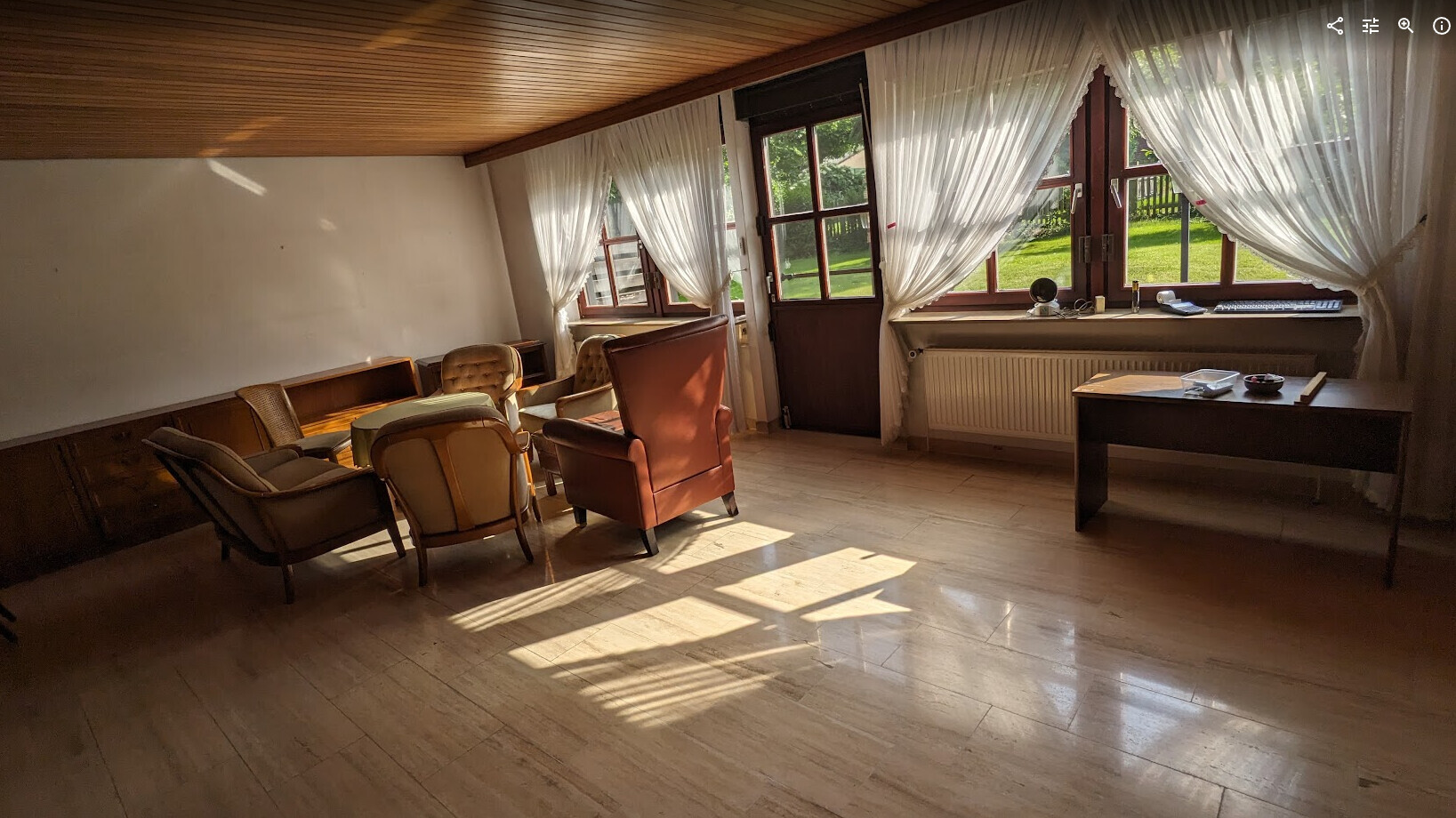 Vintage-Wohnzimmer mit mehreren bequemen Sesseln, weißen Vorhängen und Fensterblick ins Grüne.