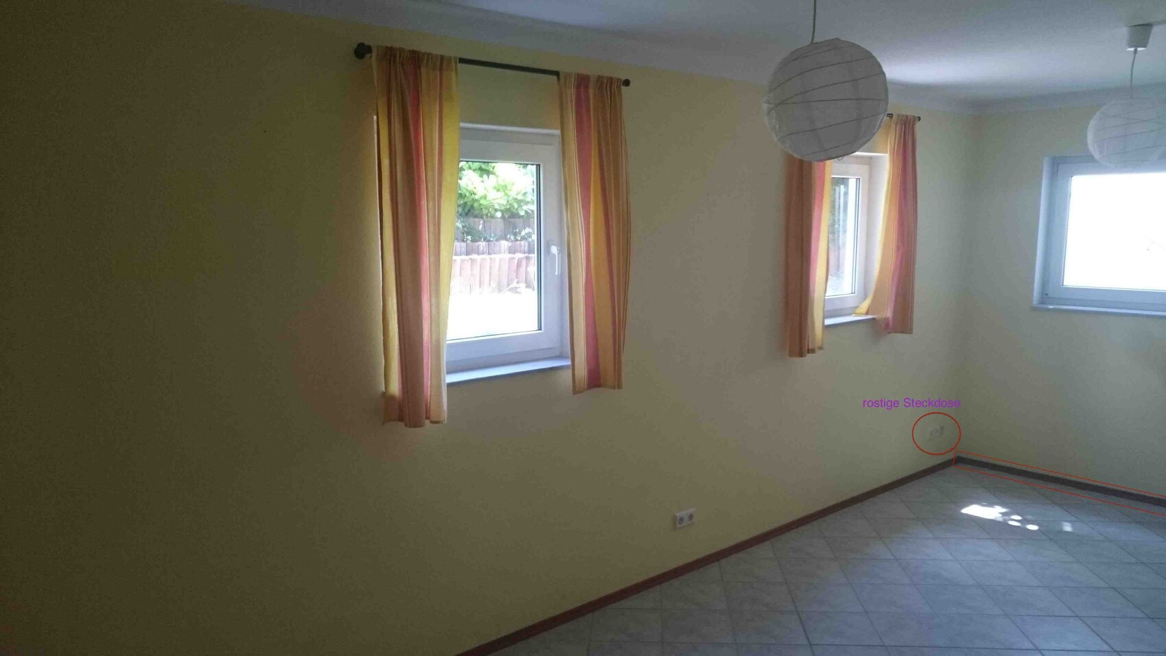 Helles Wohnzimmer mit gelben Wänden, drei Fenstern mit gestreiften Vorhängen und runden Papierlampen.