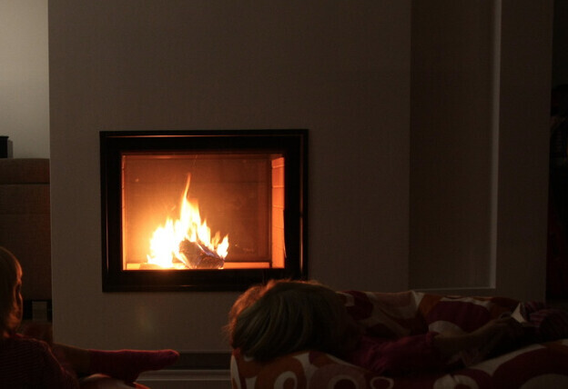 Kamin mit Flammen im Wohnzimmer; eine Person liegt entspannt auf dem Sofa.