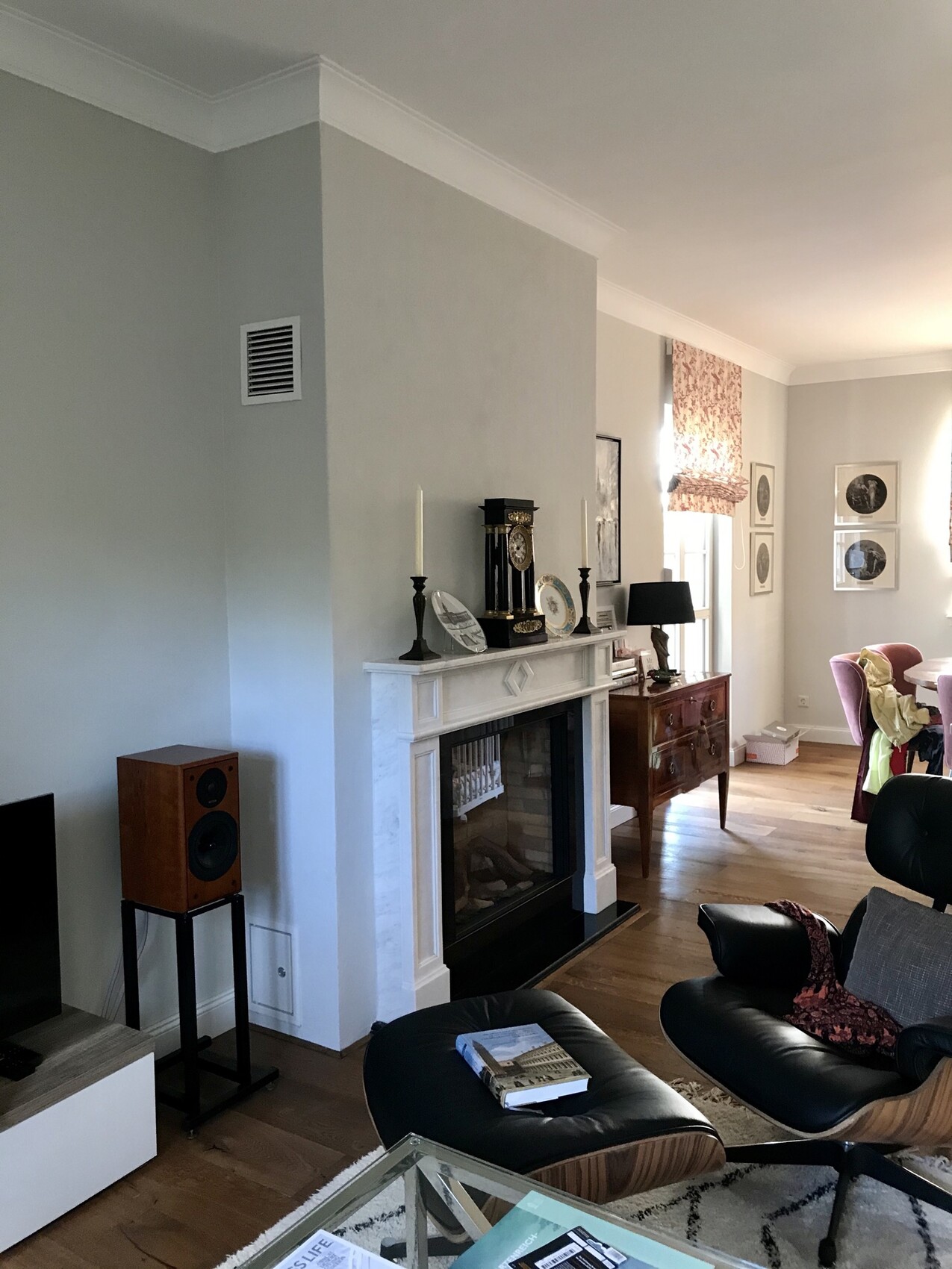 Wohnzimmer mit Kamin, Uhr auf dem Mantel, Kerzen, Leder-Sessel, Couchtisch, Bilderrahmen an der Wand.