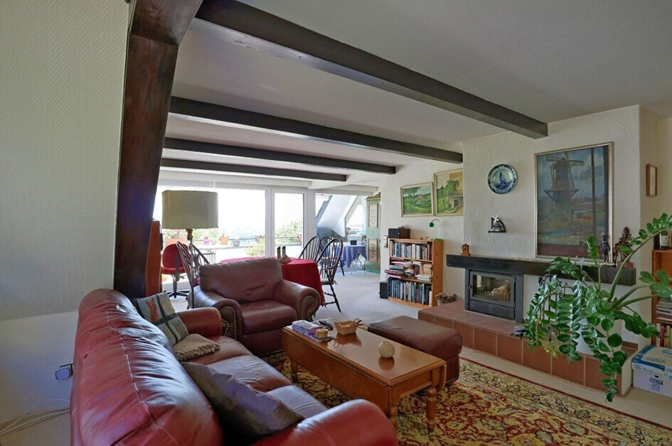 Wohnzimmer mit roten Ledersofas, Couchtisch, Bücherregal, Pflanze und Fenster mit Balkonblick.