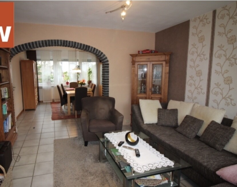 Wohnzimmer mit grauem Sofa, Sessel und Glastisch; Blick auf Essbereich durch Steinbogen.