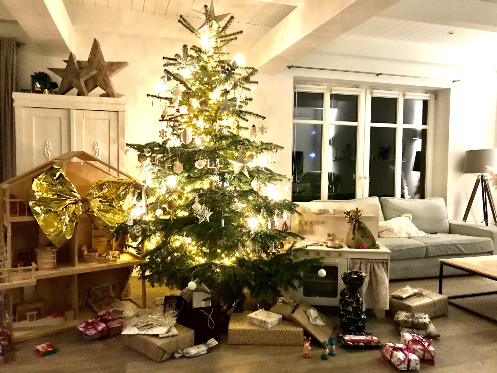 Weihnachtsbaum im Wohnzimmer mit Lichtern, Kugeln und Geschenken darunter.