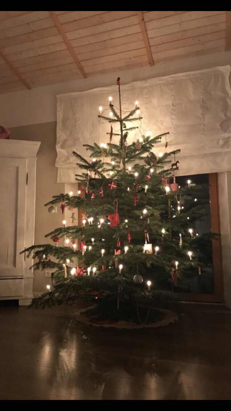 Weihnachtsbaum im Wohnzimmer mit vielen brennenden Kerzen und Dekorationen.