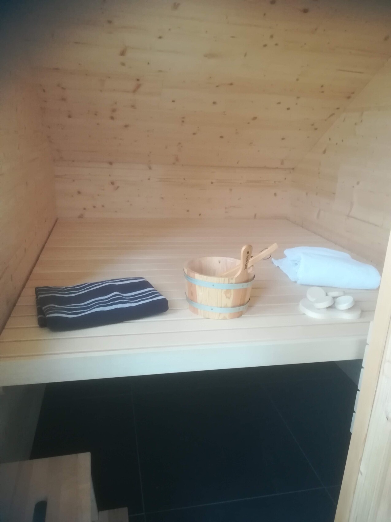 Sauna-Innenraum aus Holz mit Bank, Holzeimer und Schöpfkelle sowie Handtuch.