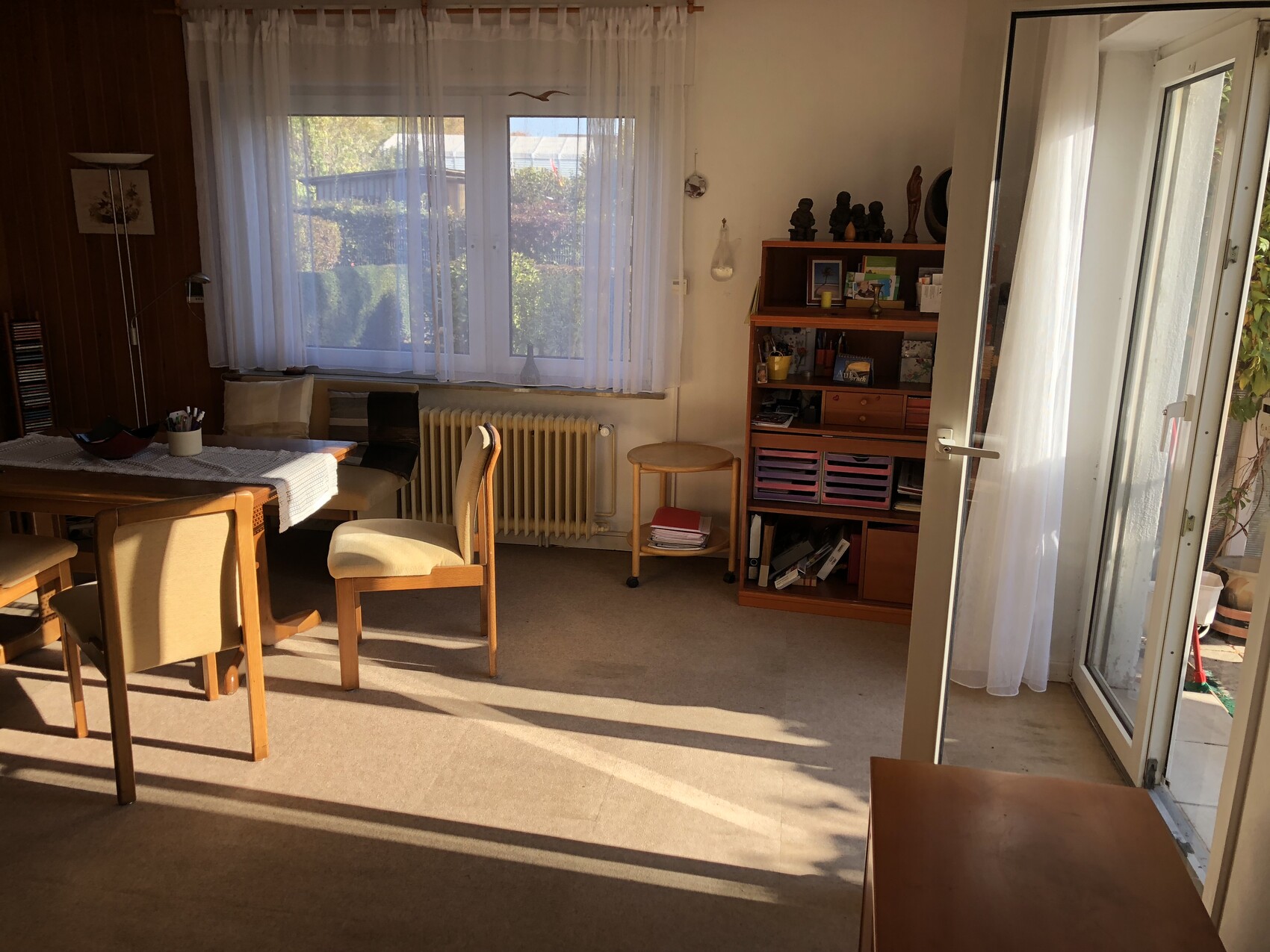 Helles Wohnzimmer mit Esstisch und Stühlen, Fensterfront mit weißen Vorhängen und Terrassentür.