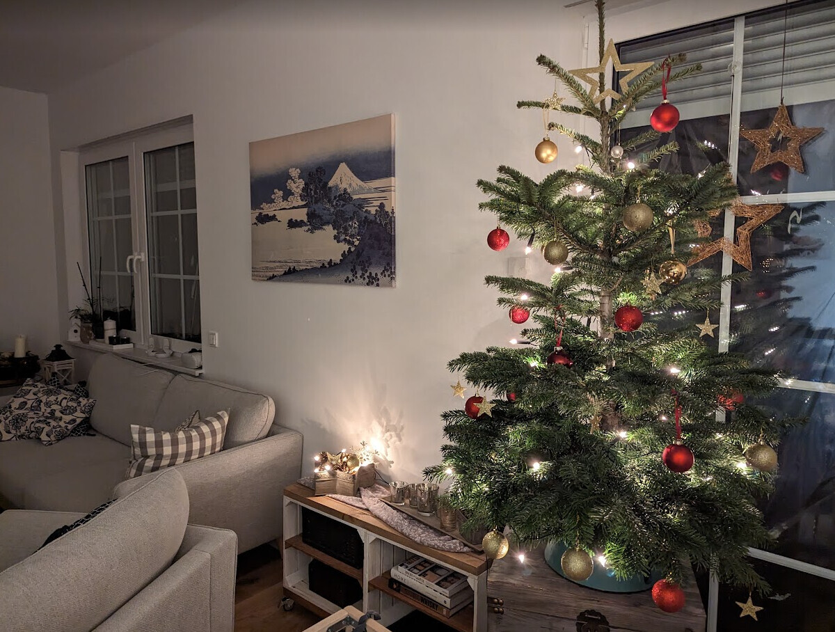 Weihnachtsbaum mit Lichterkette und roten und goldenen Kugeln im Wohnzimmer neben dem Sofa.