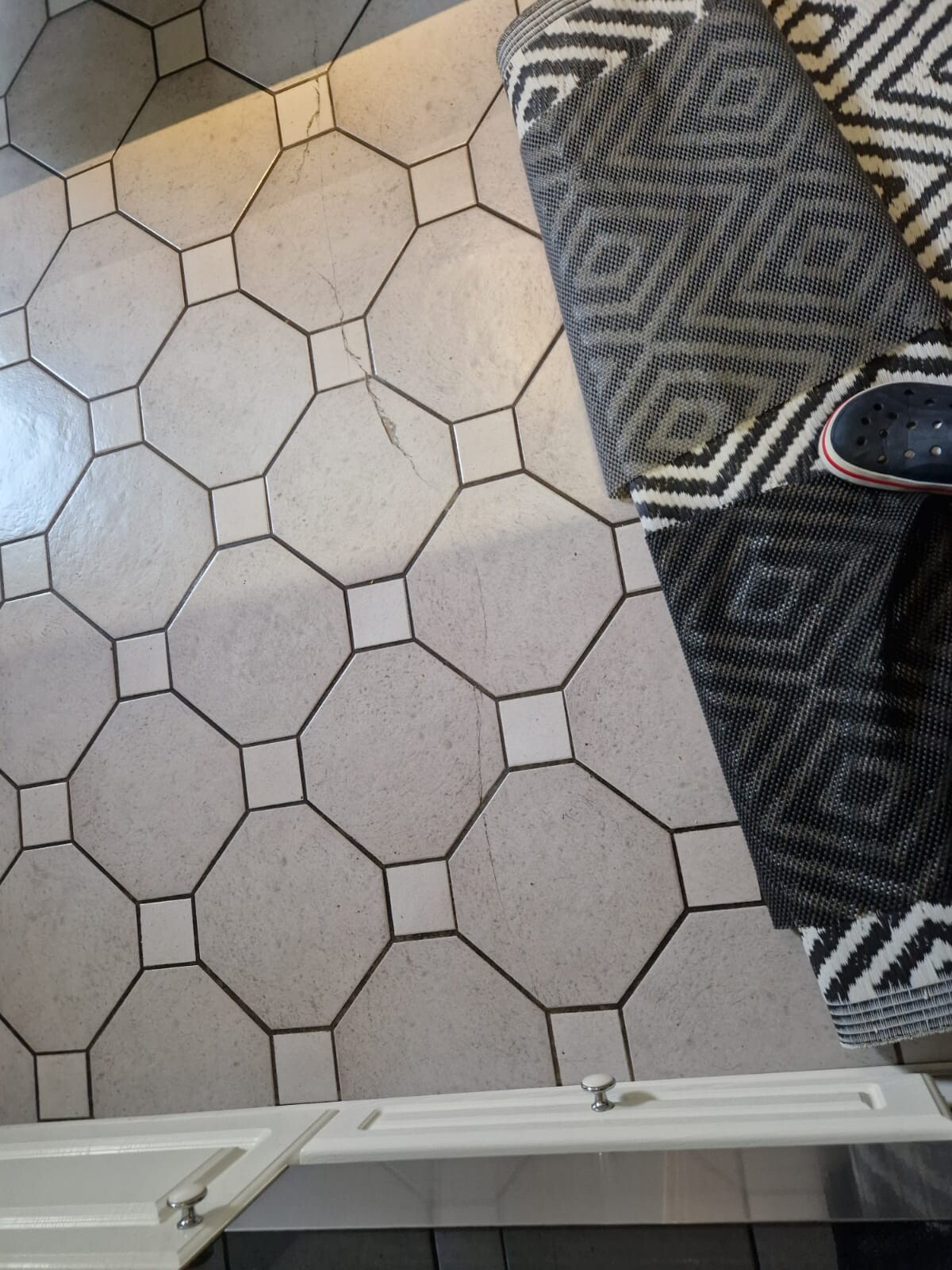 Fliesenboden mit großen Achtecken und kleinen Quadraten; rechts ein gemusterter Teppich und Crocs.