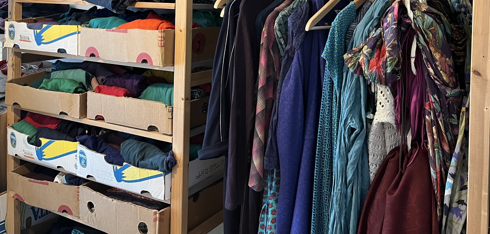 Garderobe mit bunten Kleidern an der Stange und Stoffen in Kartons auf Regalen.