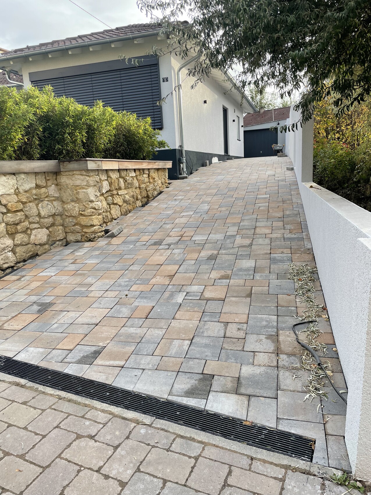 Pflasterweg führt zu einem weißen Einfamilienhaus, Steinmauer links, Garage im Hintergrund.