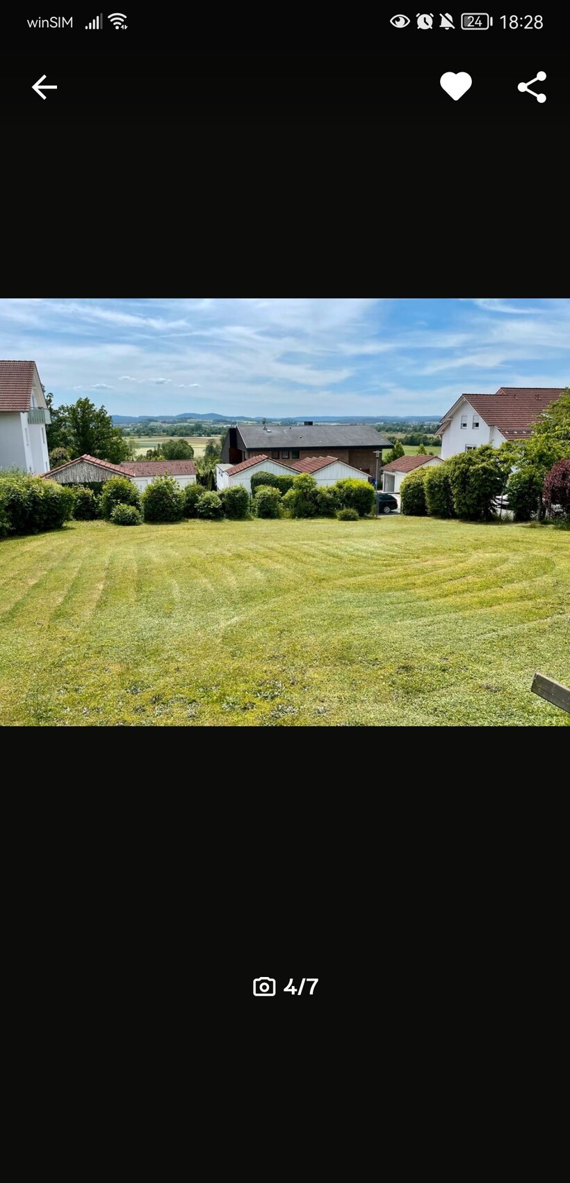 Gepflegter Garten mit Rasen, Hecken und Häusern im Hintergrund unter blauem Himmel