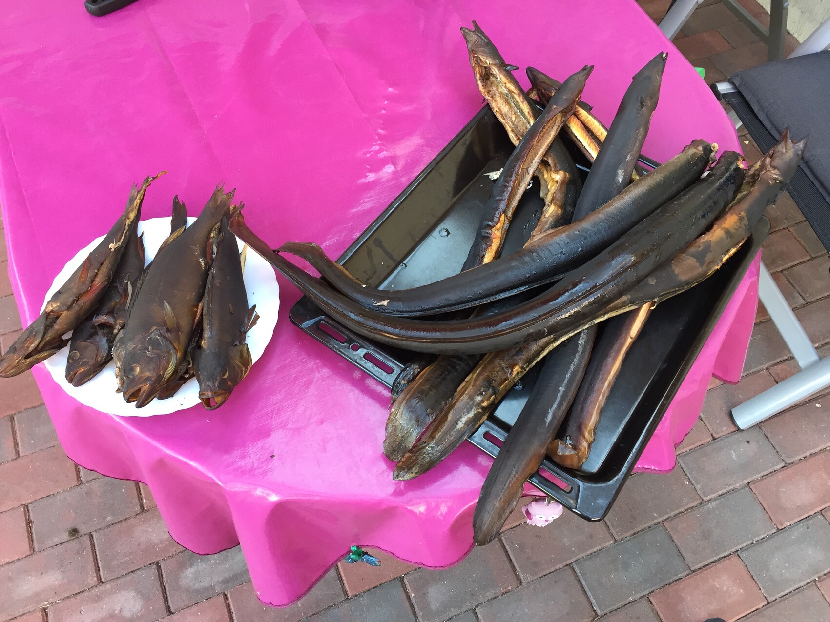 Mehrere lange geräucherte Fische liegen auf einem Backblech; pinker Tisch im Hintergrund.
