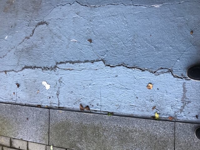 Rissige blaue Betonfläche mit Gehwegplatten, Schuh am rechten Rand.