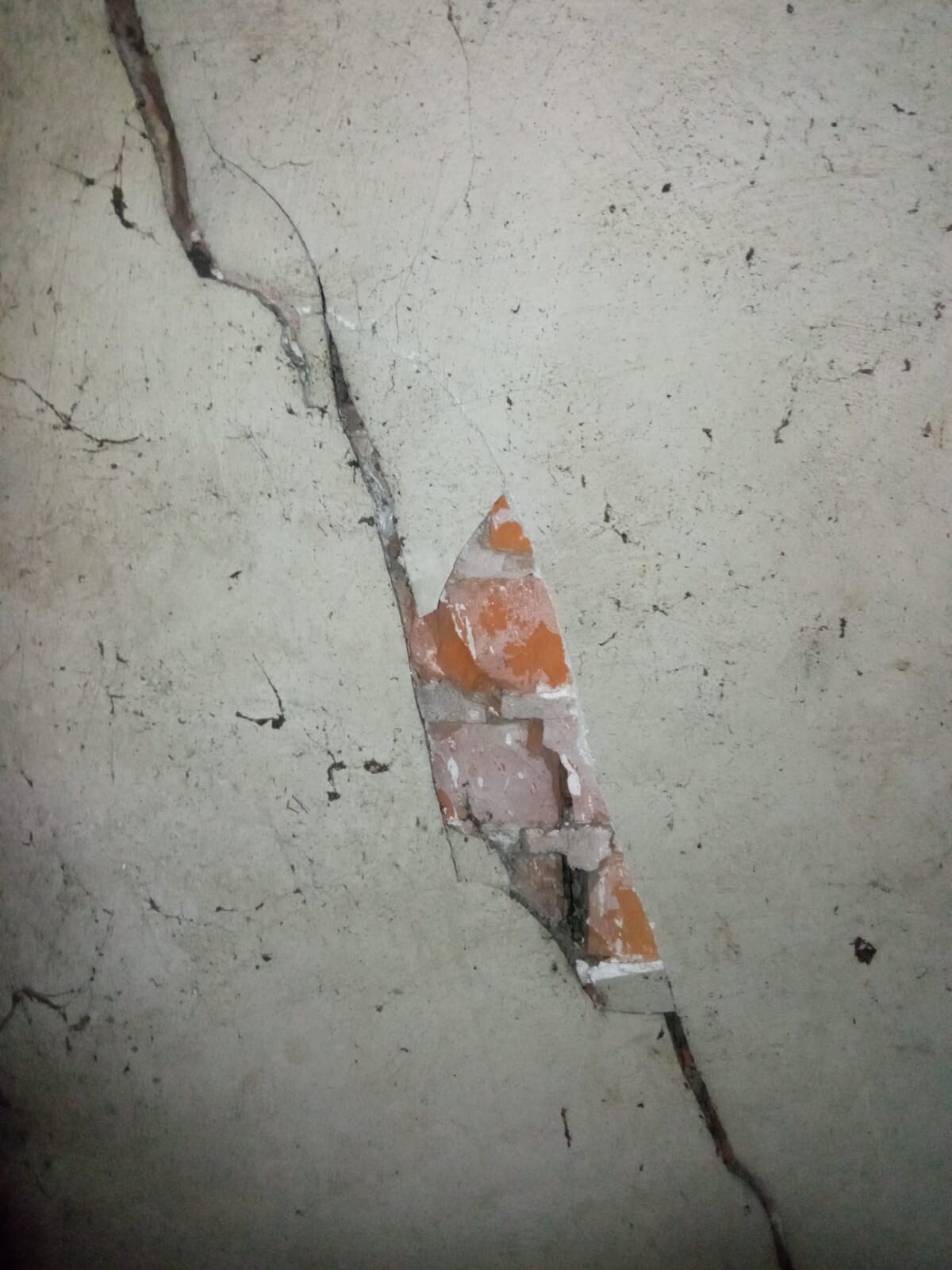 Großer Wandriss mit freigelegten orangefarbenen Ziegeln hinter Putz.