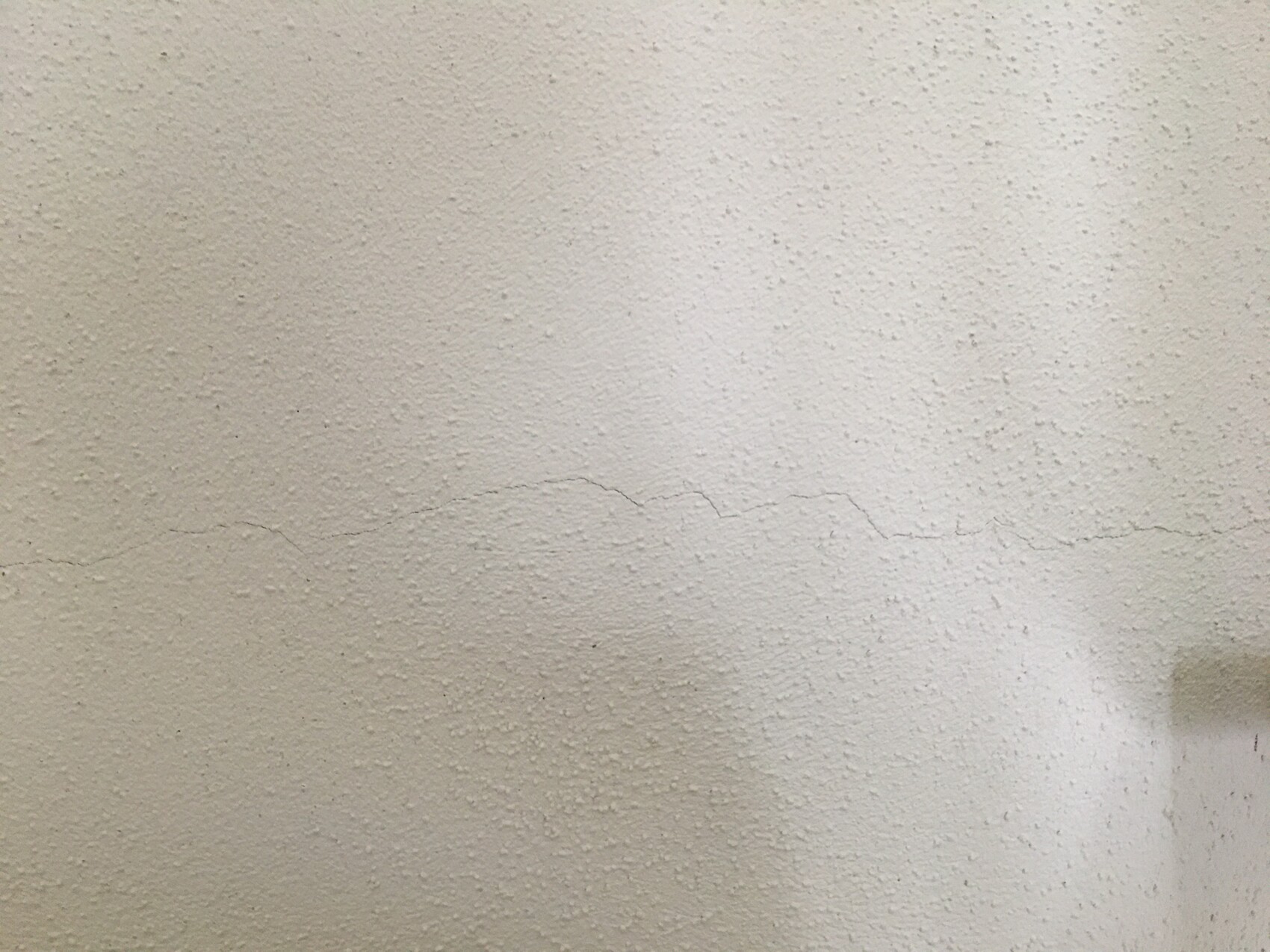Weiße, strukturierte Wand mit einer feinen horizontalen Risslinie.