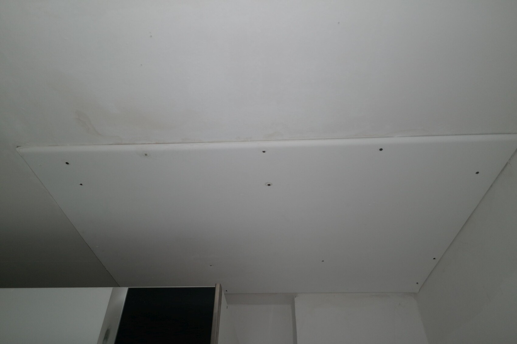 Weiße Rigips-Deckenverkleidung mit sichtbaren Schraubenköpfen, Blick auf den Raumwinkel.