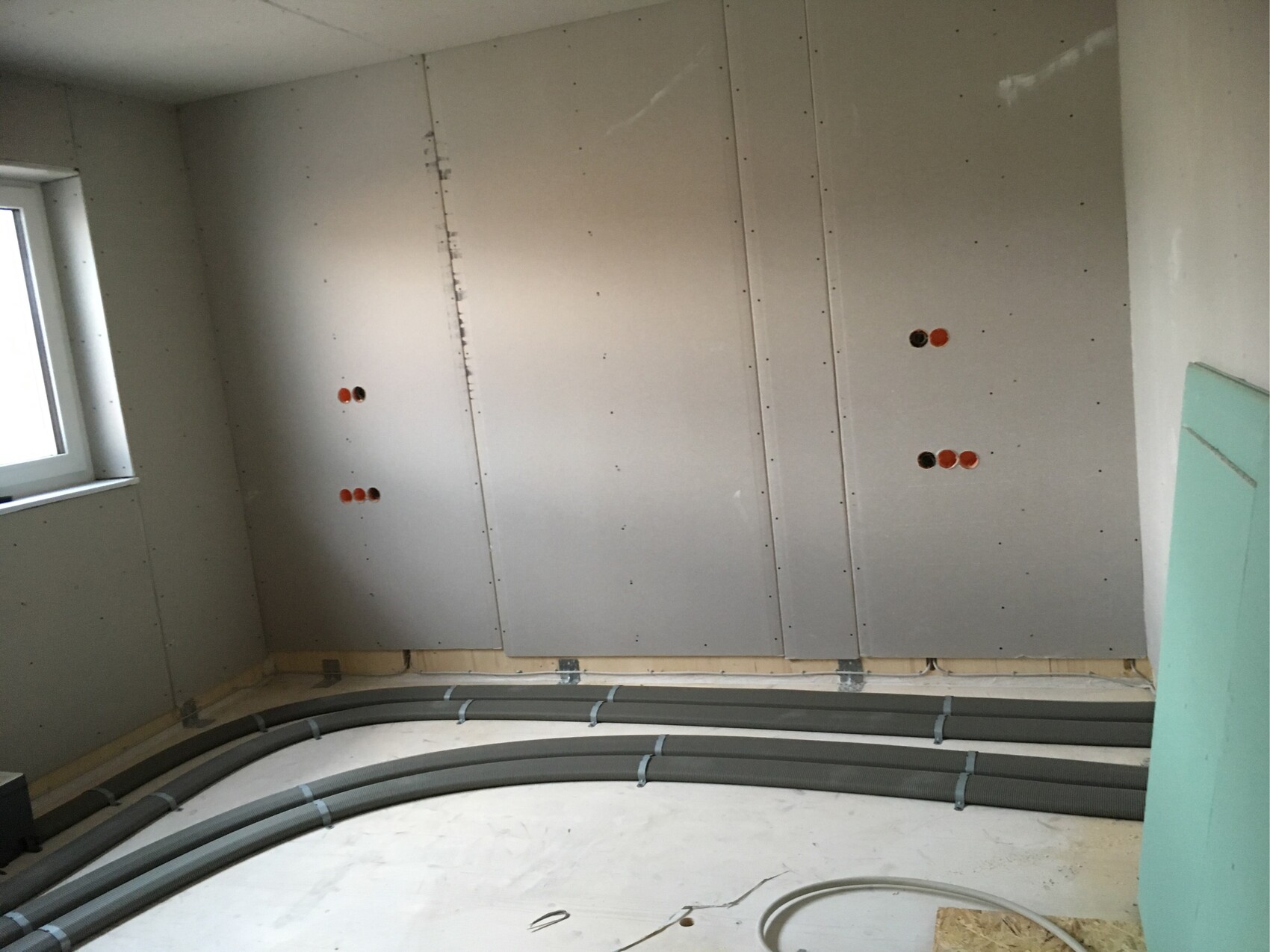 Rohbauzimmer: Gipskartonplatten an Wänden, orange Steckdosenlöcher, Kabelrohre am Boden.