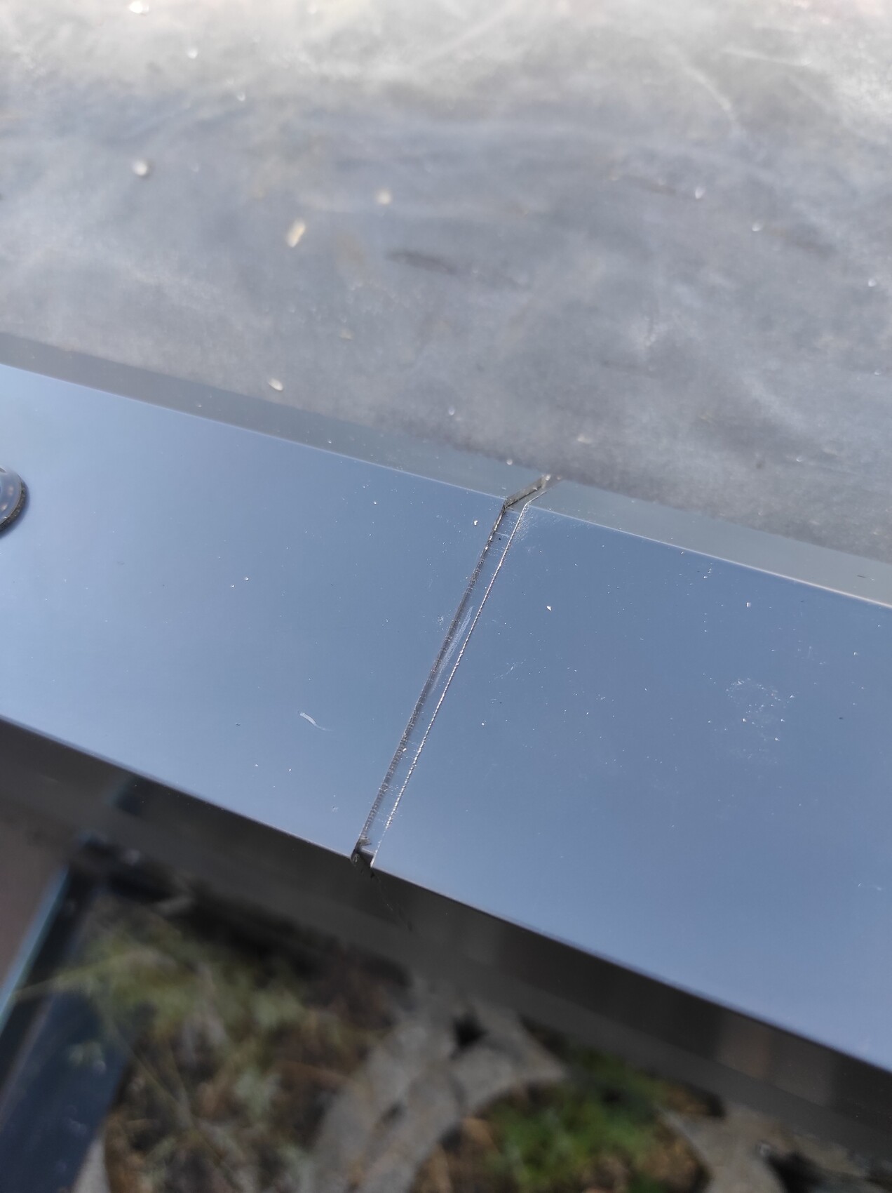 Nahaufnahme einer dunklen Metallkante mit einer senkrechten Fuge am Rand der Platte, draußen.
