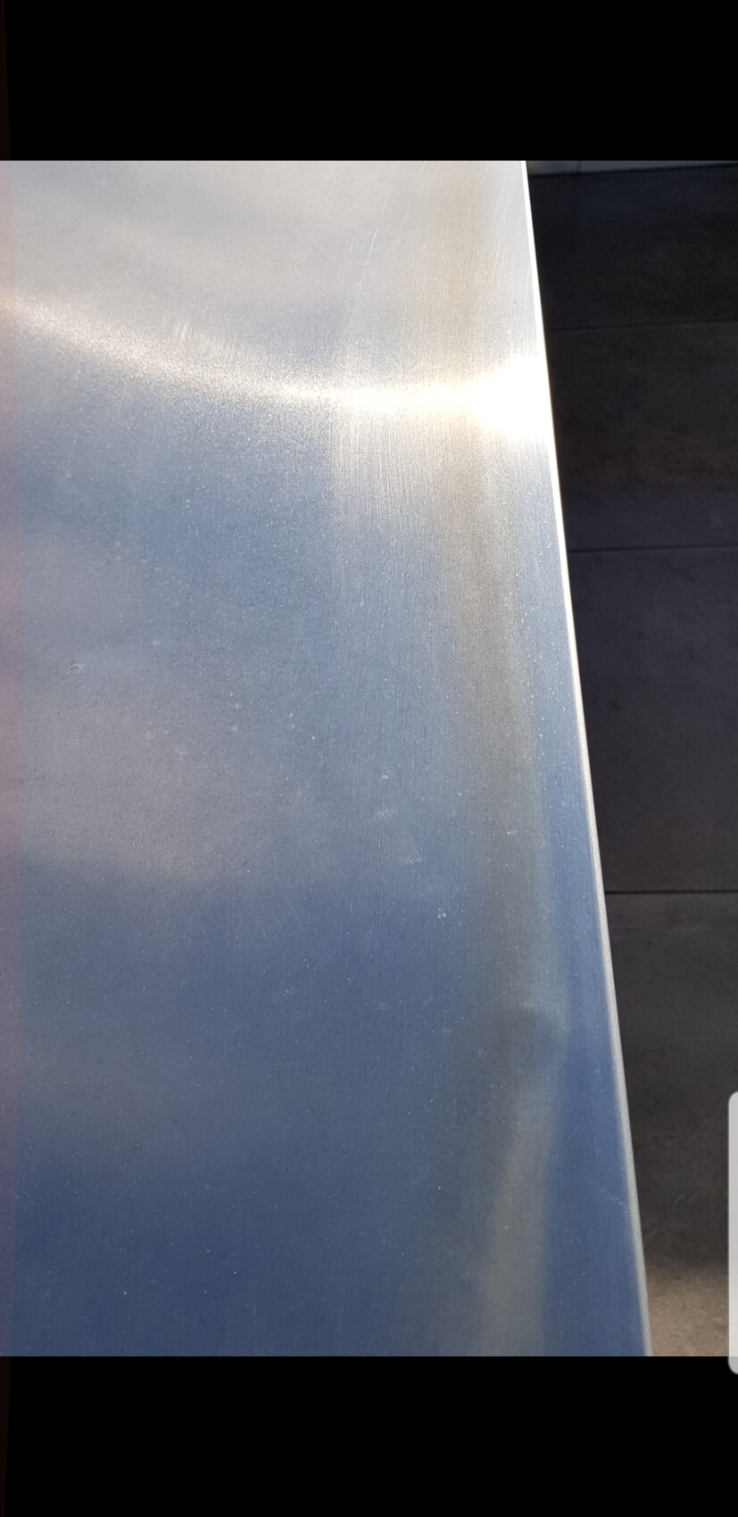 Nahaufnahme einer silbernen Metalloberfläche mit leichter Struktur und Lichtreflexen.