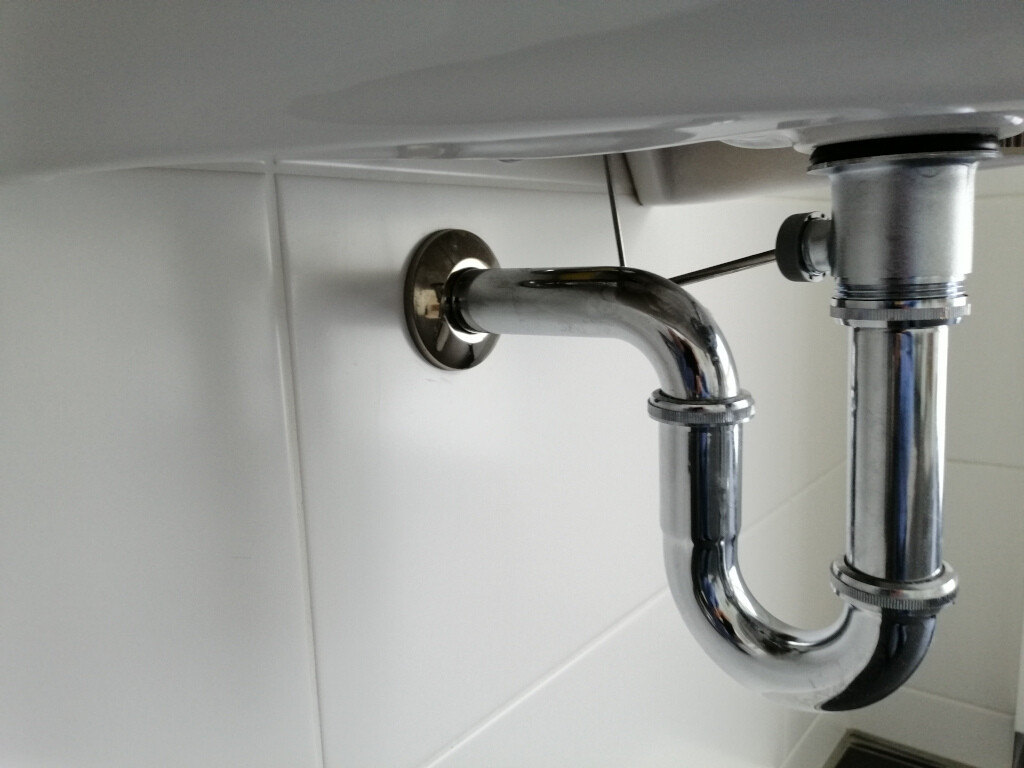 Unter dem Waschbecken sichtbarer Chrom-P-Trap aus Metall mit U-förmigem Abfluss und Wandanschluss.