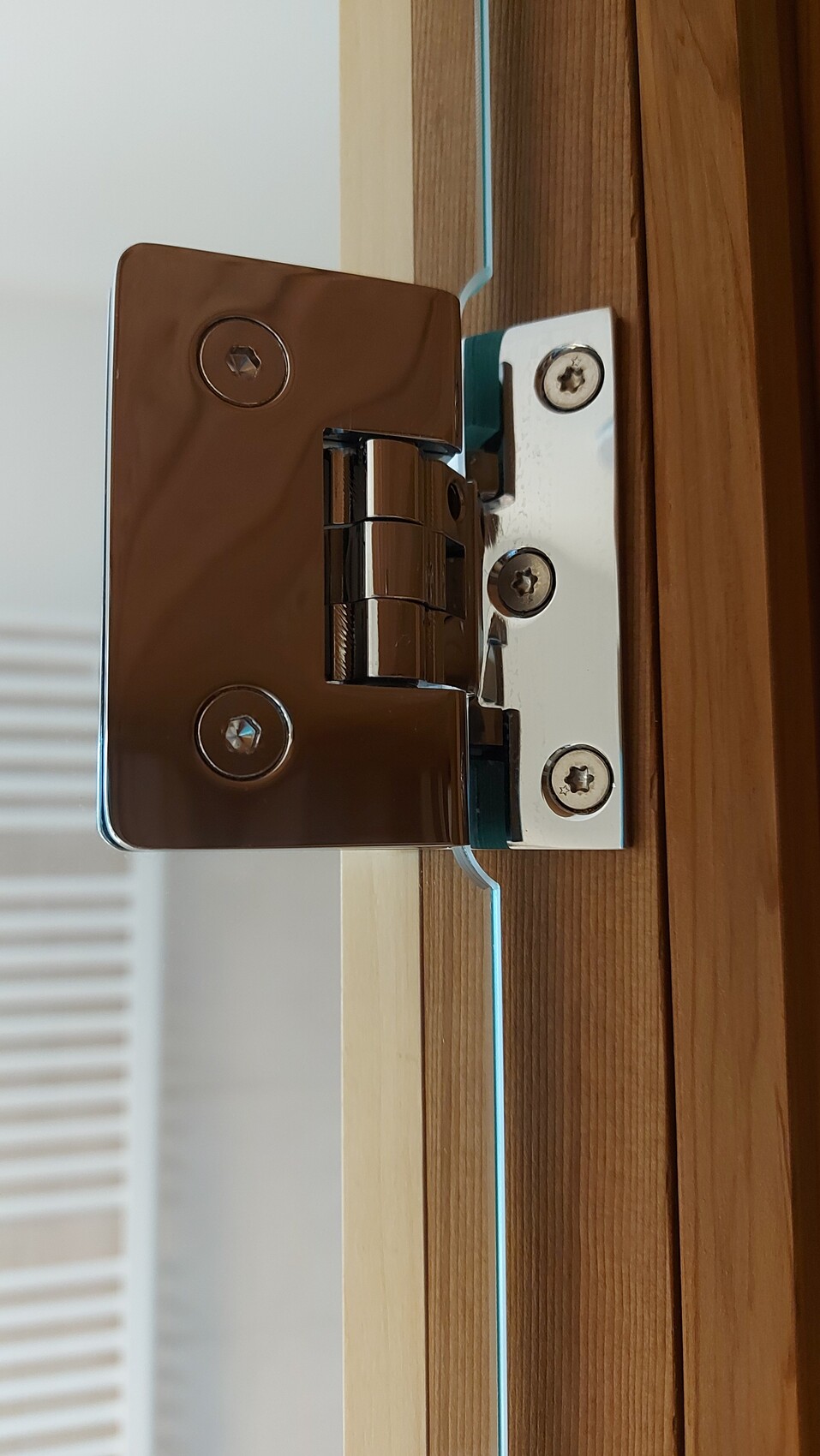 Nahaufnahme eines Türscharniers aus Metall an einem Holztürrahmen mit Schrauben.