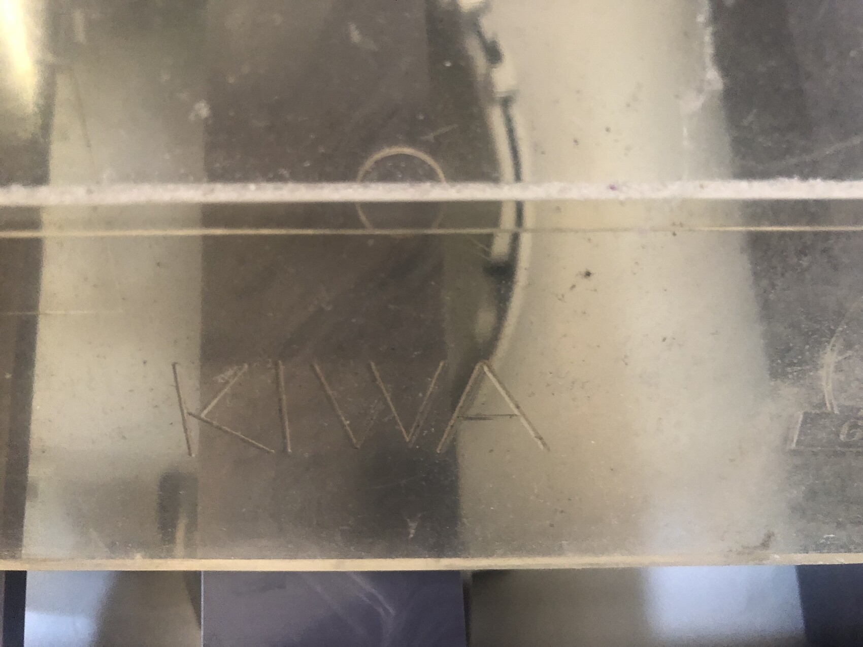 Nahaufnahme einer staubigen Metalloberfläche mit eingeritzten Buchstaben unten links.