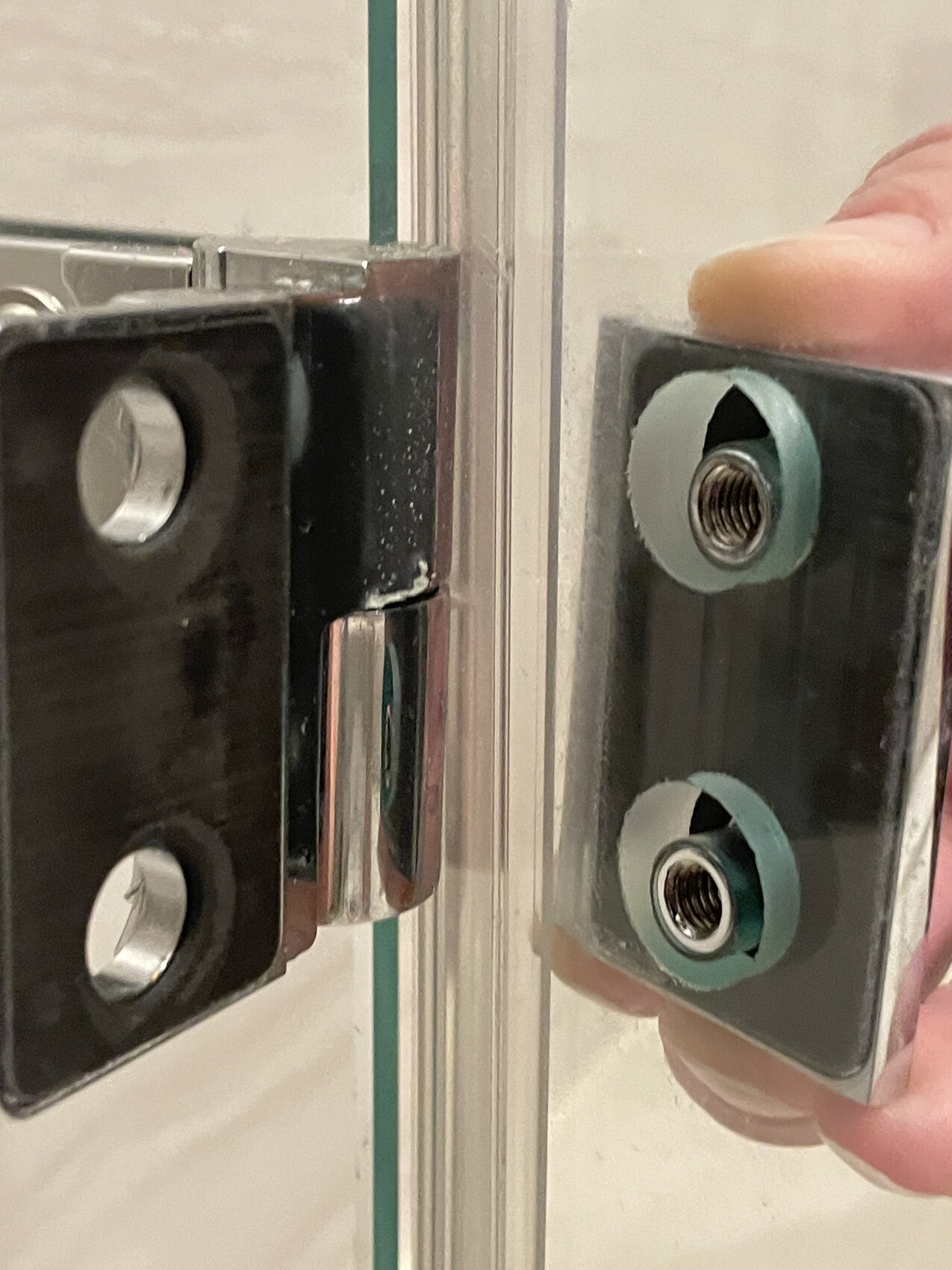 Nahaufnahme eines Glas-Türbeschlags: linkes schwarzes Bauteil, rechte Platte mit Gewinden.