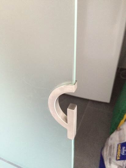 Glas-Schranktür mit weißem, C-förmigem Metallgriff; Türspalt sichtbar.