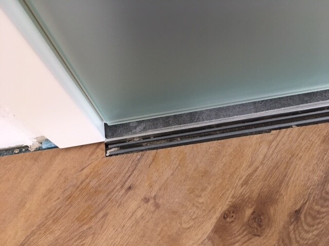 Nahaufnahme einer Glasschiebetür mit schwarzer Metallschiene am Holzboden.