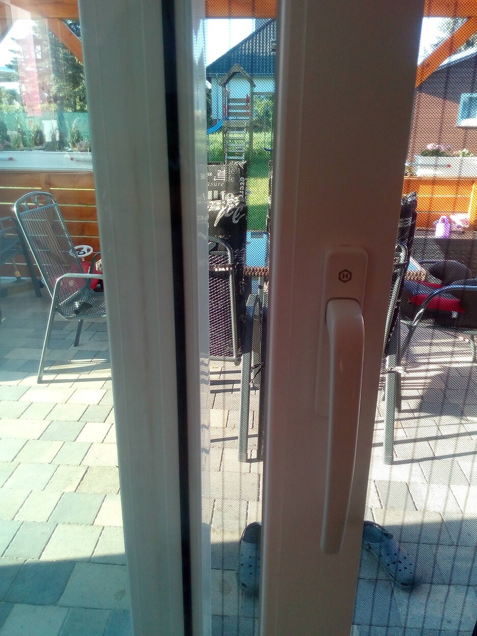 Blick durch eine Glasschiebetuer auf Garten mit Gartenmoebel und Stuehlen