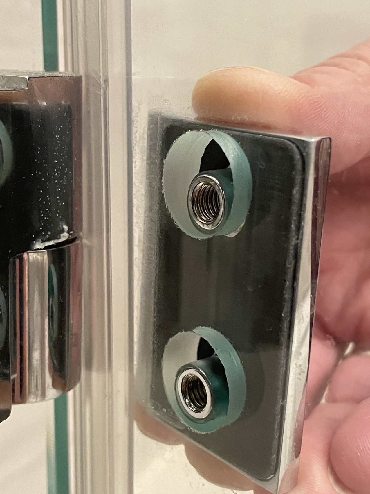 Nahaufnahme eines Glastür-Beschlags mit zwei grünen Dichtungsringen um Metall-Gewinde.